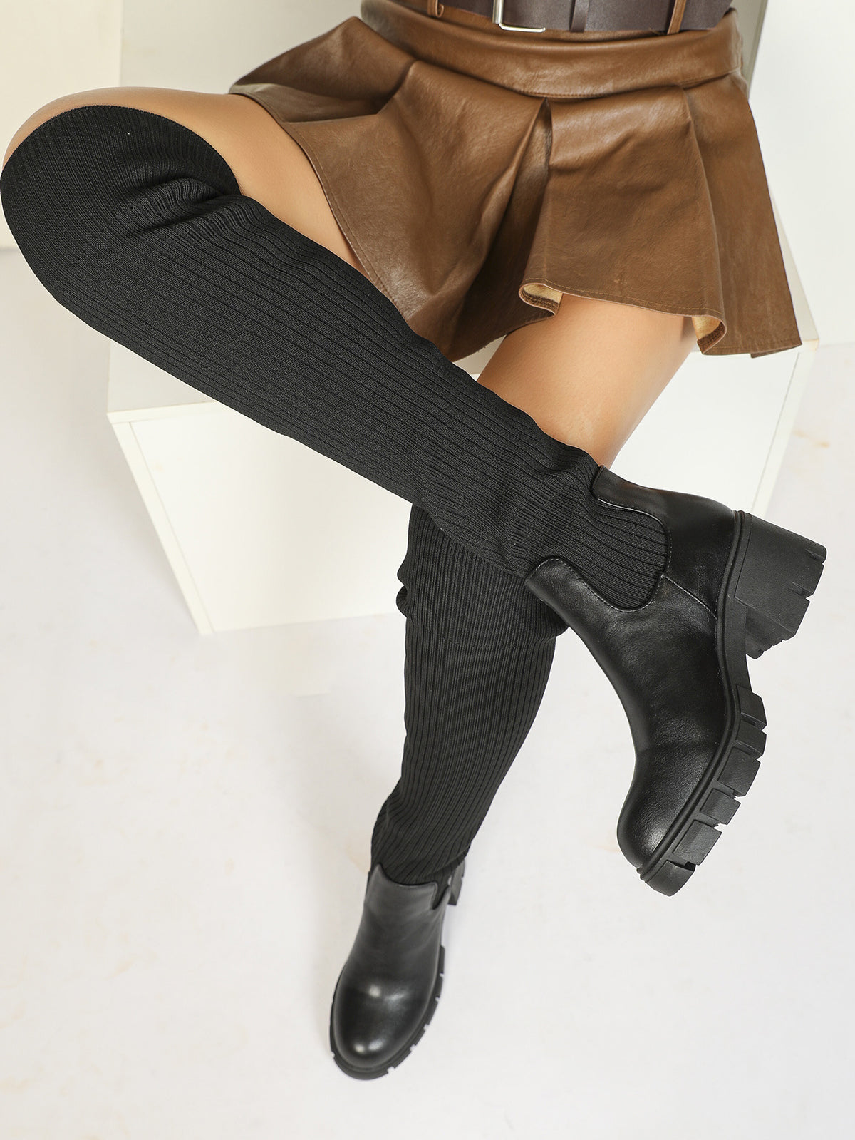 Mescini black ribbed knit over the knee platform boots, worn by a model reclining in a skirt, US women's sizes